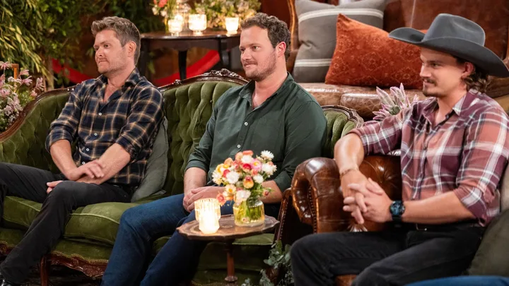 Three men dressed in shirts and jeans sitting on a couch.