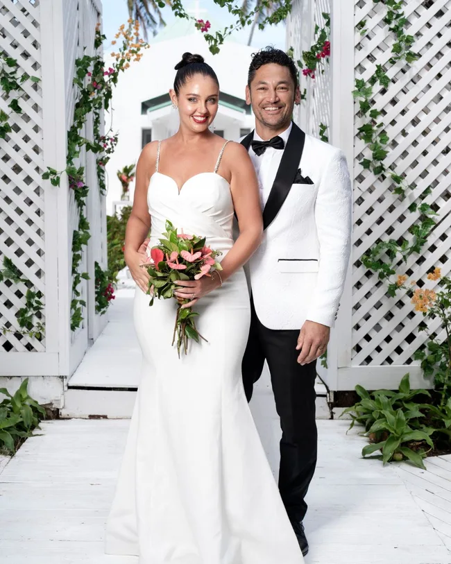 A man and woman dressed in wedding attire standing and smiling on a beach.
