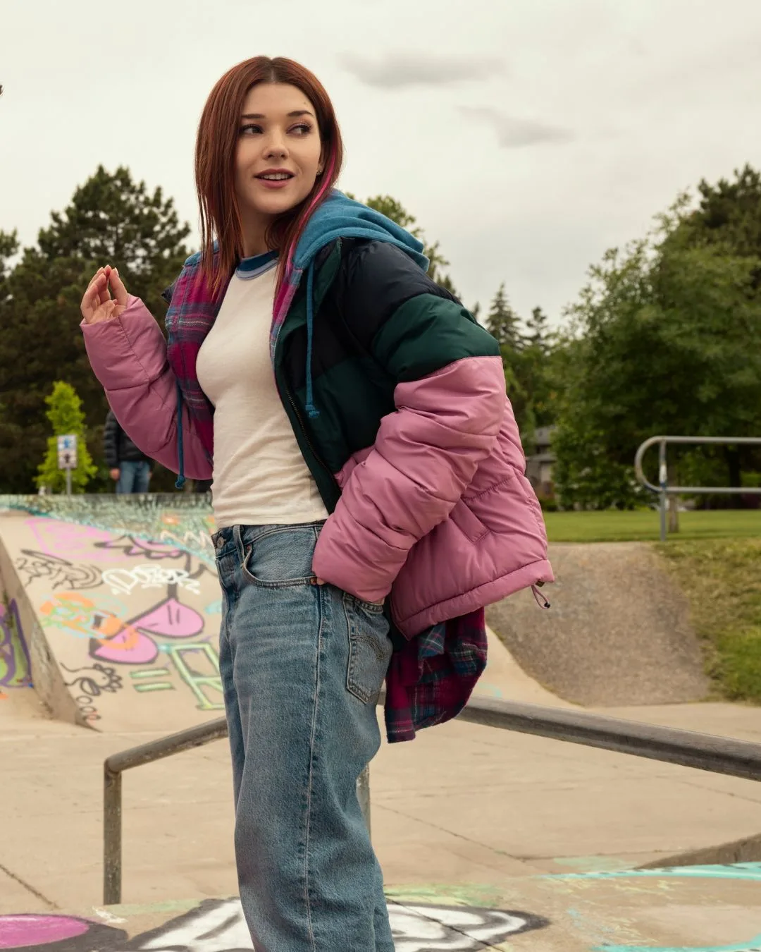 A woman wearing a puffer jacket and jeans smiling.