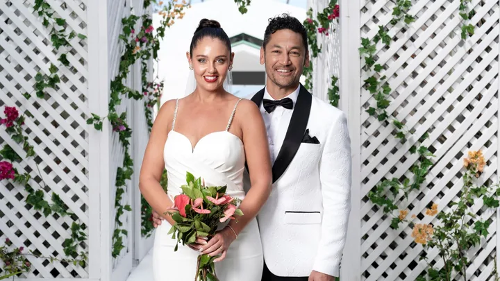 A man and woman dressed in wedding attire standing and smiling on a beach.