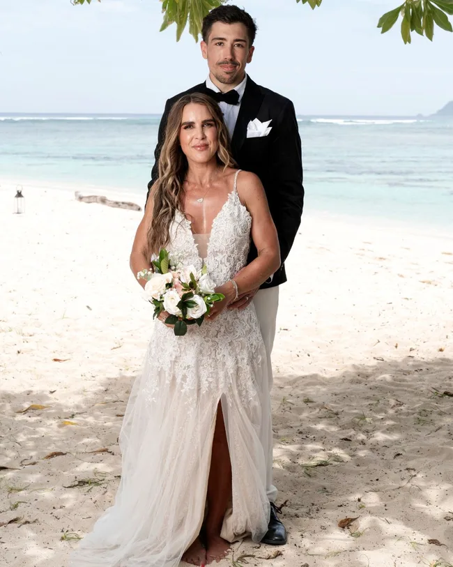 A man and woman dressed in wedding attire standing and smiling on a beach.