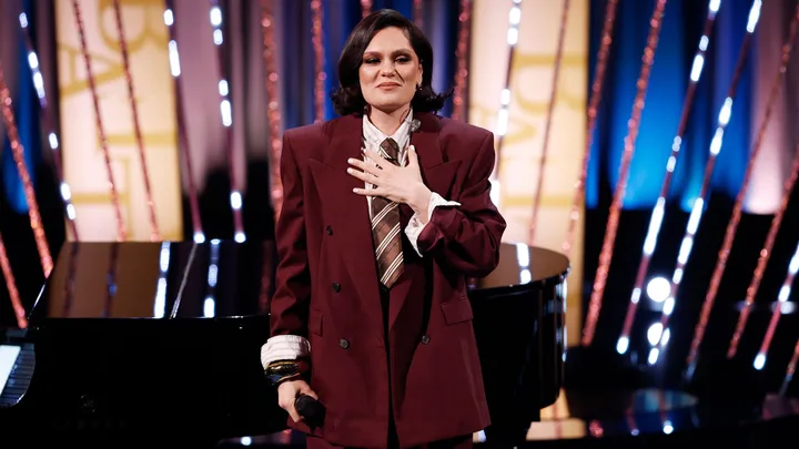 A woman wearing a burgundy suit holding her hand to her chest.