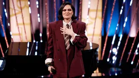 A woman wearing a burgundy suit holding her hand to her chest.