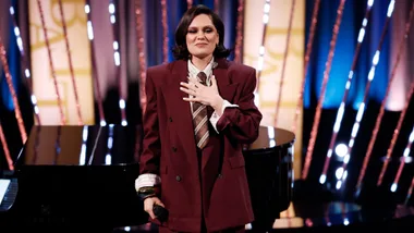 A woman wearing a burgundy suit holding her hand to her chest.