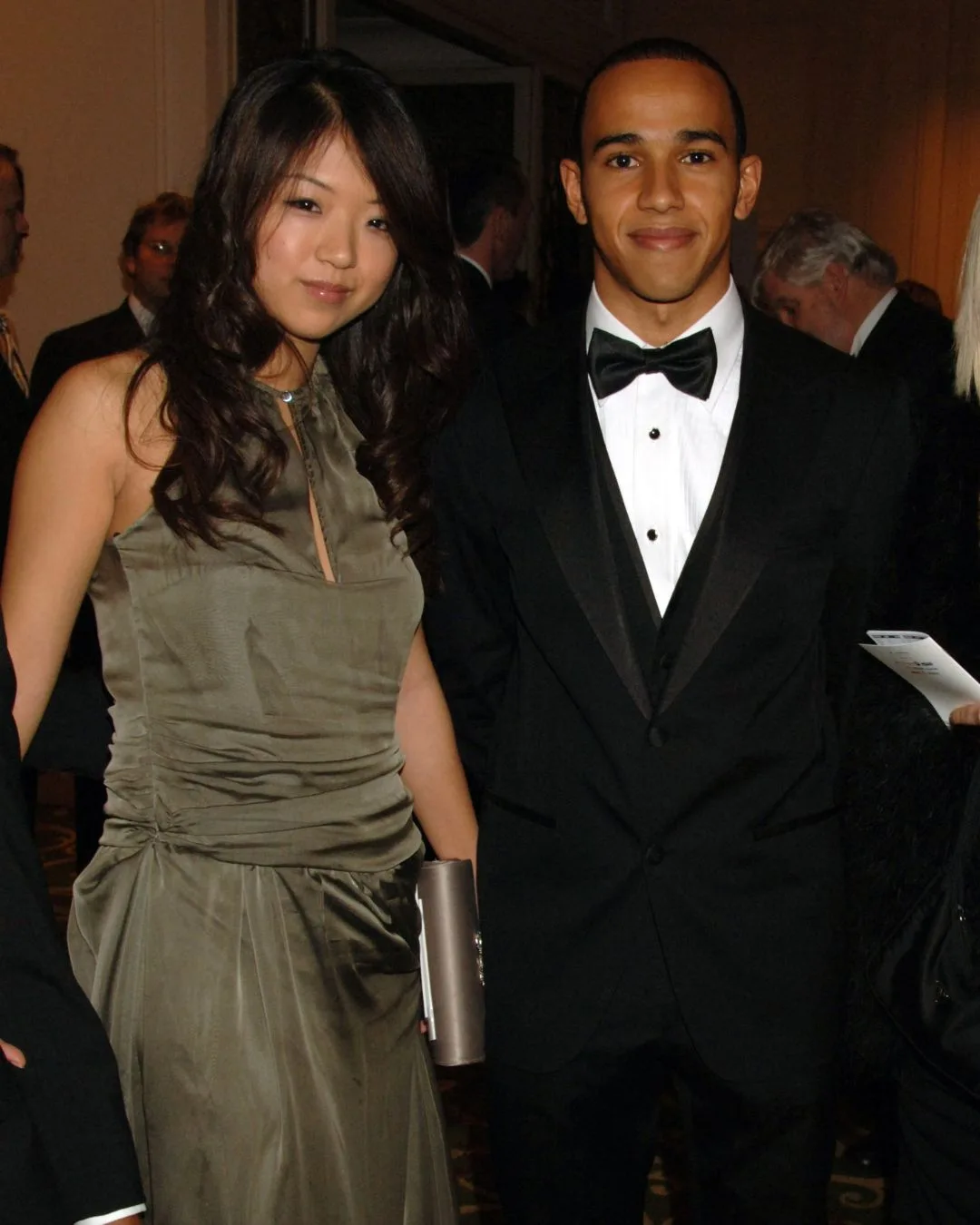 A man wearing a tuxedo smiling next to a woman with long brunette hair and a green silk dress. 