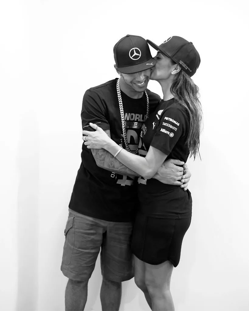 A man and woman dressed in athletic wear and baseball hats kiss each other on the cheek.