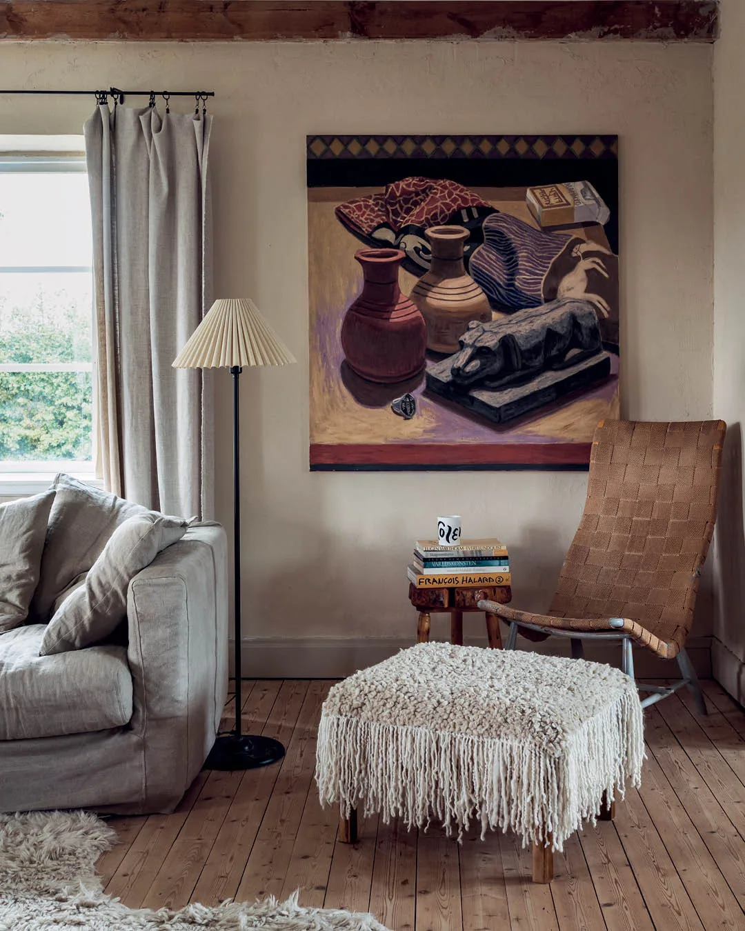 A neutral coloured living room with a large still life painting on the wall. 