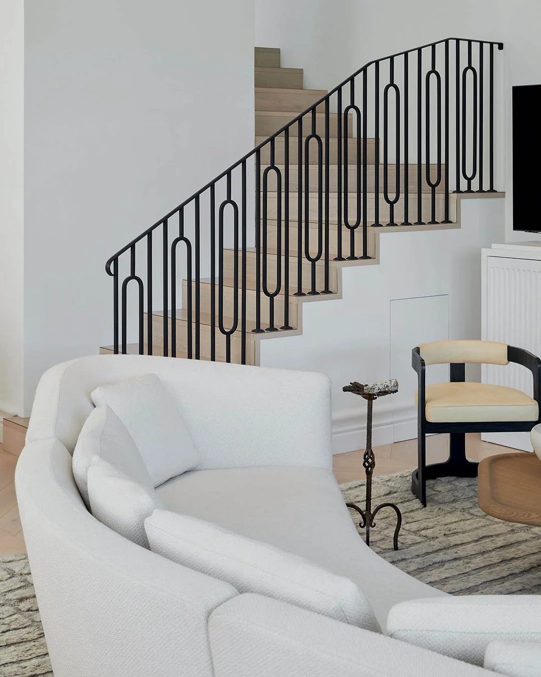 A curved white sofa in a living room. A staircase framed with sculptural railings is in the background. 