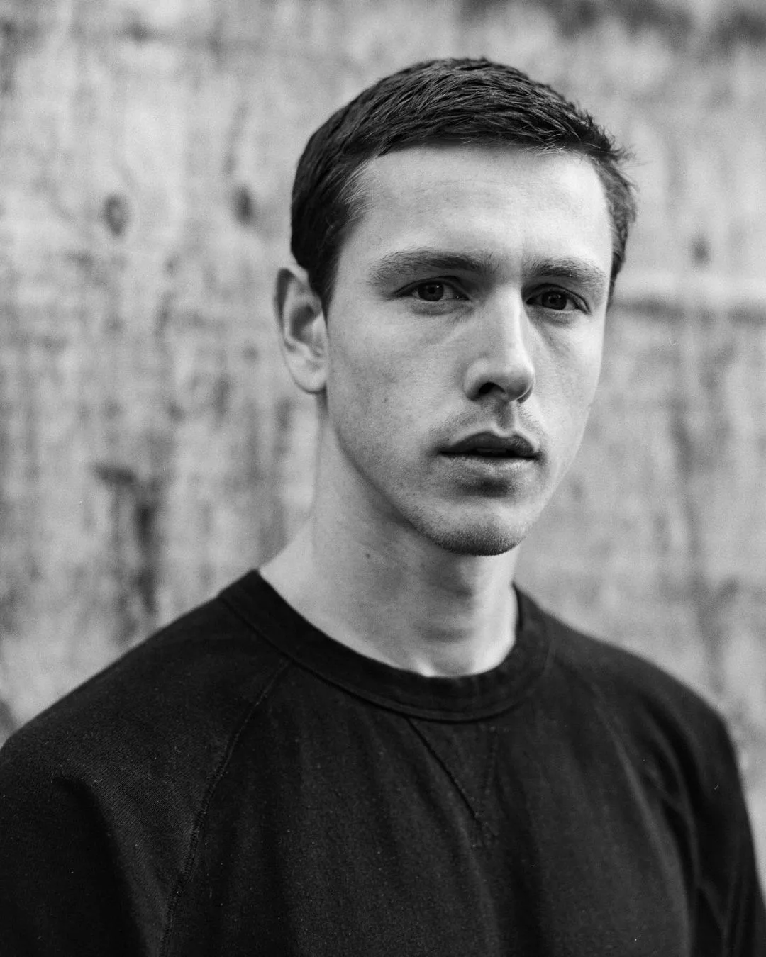 A black and white portrait of a young man with short hair and a black jumper.