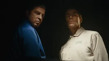 Two men stand obscured by shadows wearing polo jumpers.