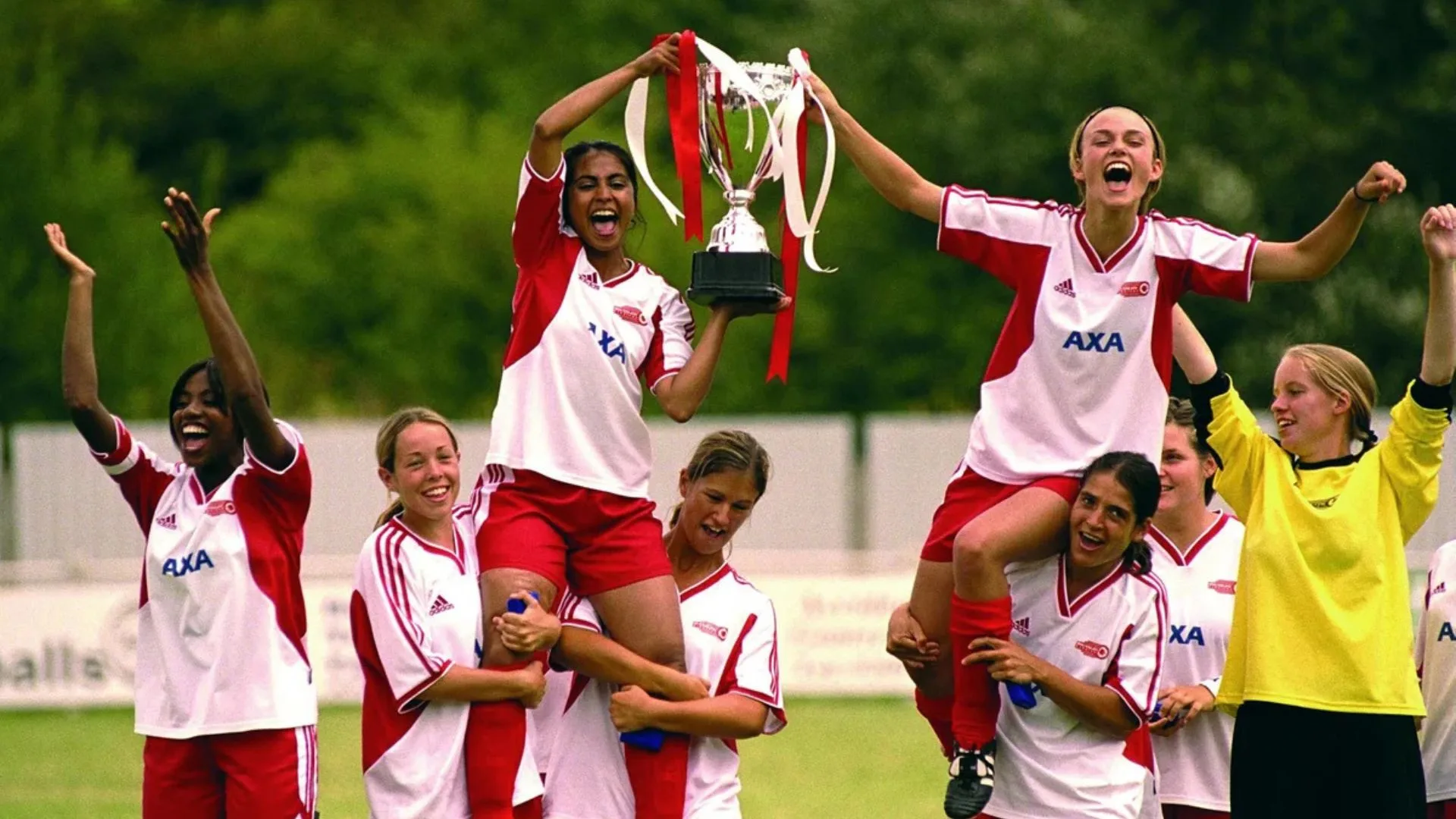 Bend It LIke Beckham 2 film still showing a group of women celebrating a competition win by cheering and holding up a trophy. 