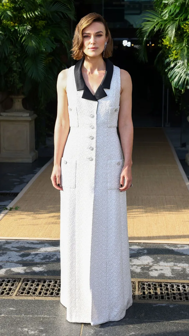 A woman with short hair wearing a white floor-length dress with black collar.