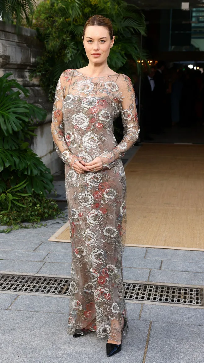 A woman wearing a sheer floor length, long sleeved gown with floral embellishments.