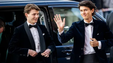 Two young men wearing tuxedos waving and smiling.