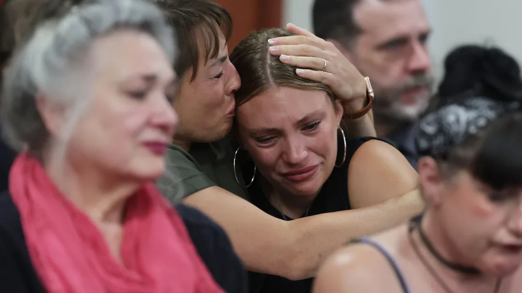 A young woman crying, who is being comforted by her mother in a courtroom audience.