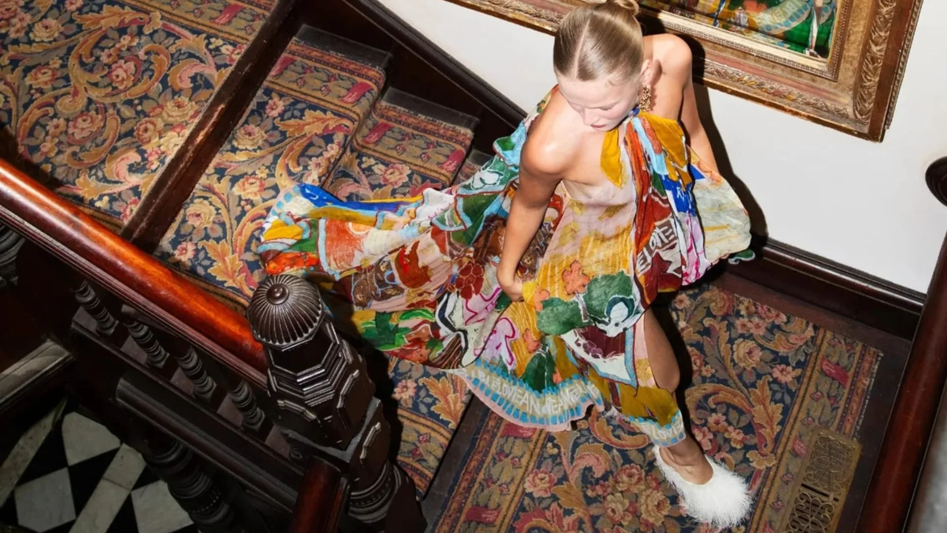 Model wears colourful wedding guest dress while walking down hotel stairs in photoshoot for Alemais