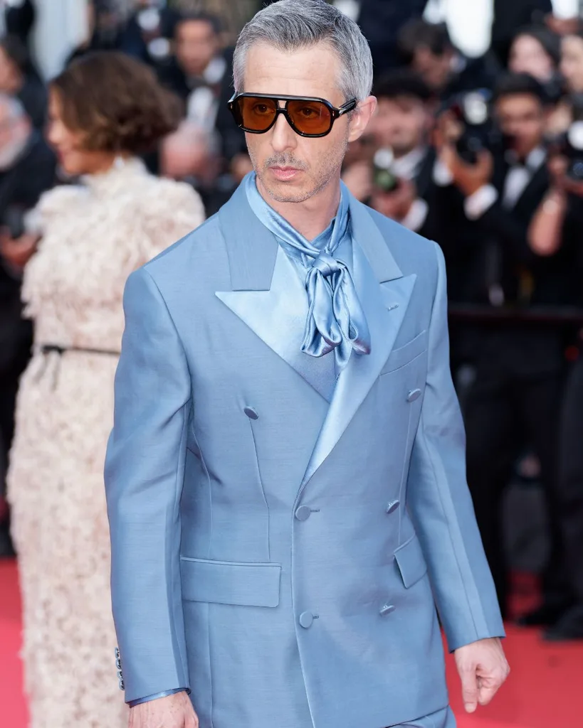 A man wearing a blue suit and orange tinged sunglasses on the Cannes red carpet.