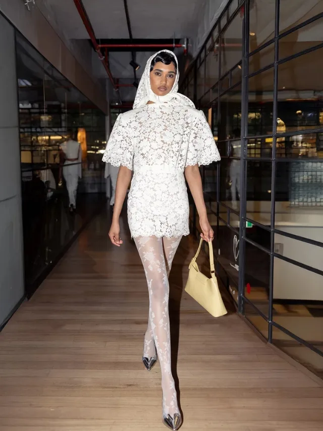 Woman wears a lace mini wedding dress with lace tights and a lace bonnet at a restaurant