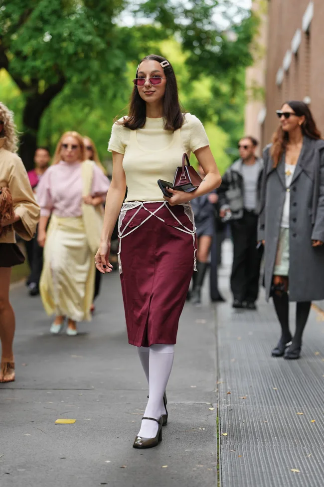 Milan Fashion Week houlder-length dark brown hair with a center part and a rectangular pale pink hair clip, small oval pink-tinted sunglasse