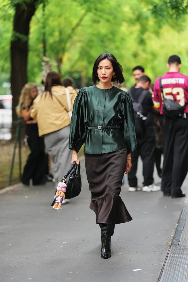 Molly Chiang wears a chin-length straight black bob with a slight side part, gold triangular drop earrings and a gold bracelet, a black leather slouchy shoulder bag from Fendi with a purple / pink / orange