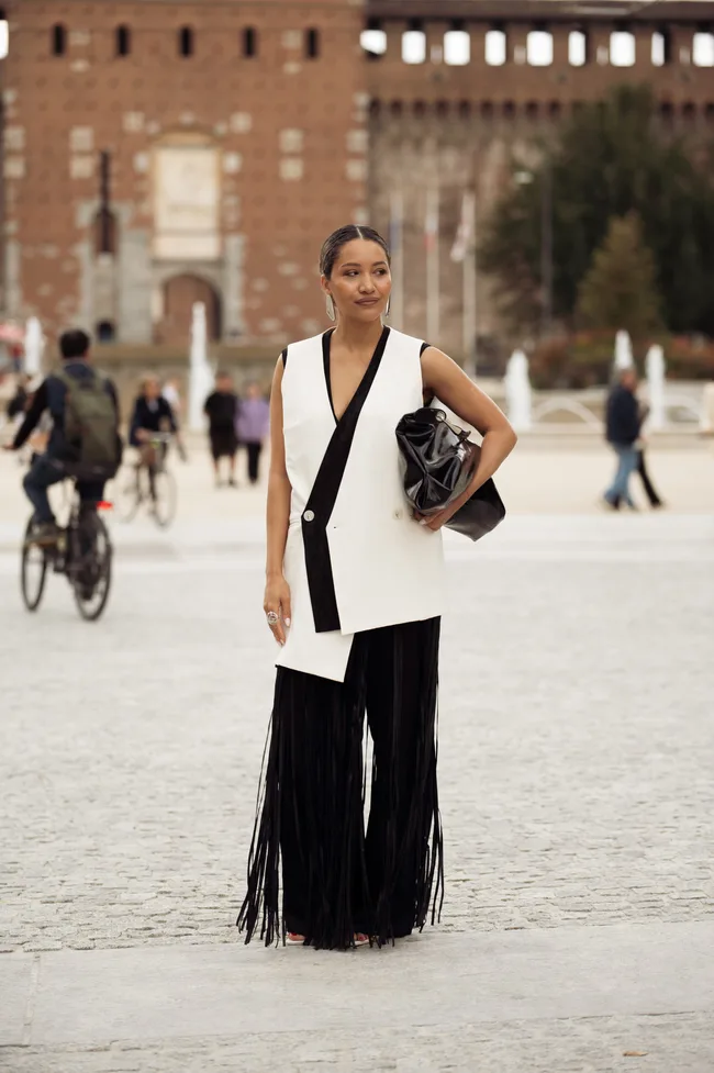 A guest wears a sleeveless black and white wrap vest with black fringe trousers