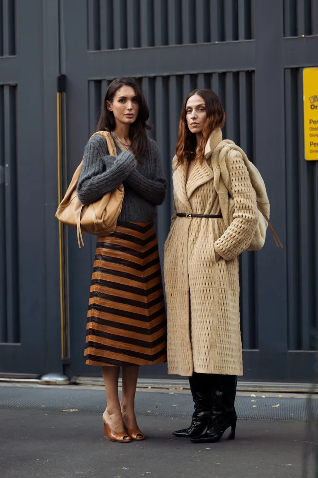 Diletta Bonaiuti wears a grey v-neck sweater with a metallic copper and black striped leather midi skirt, tan bag, and brown peep-toe heels and Erika Boldrin wears a textured beige belted