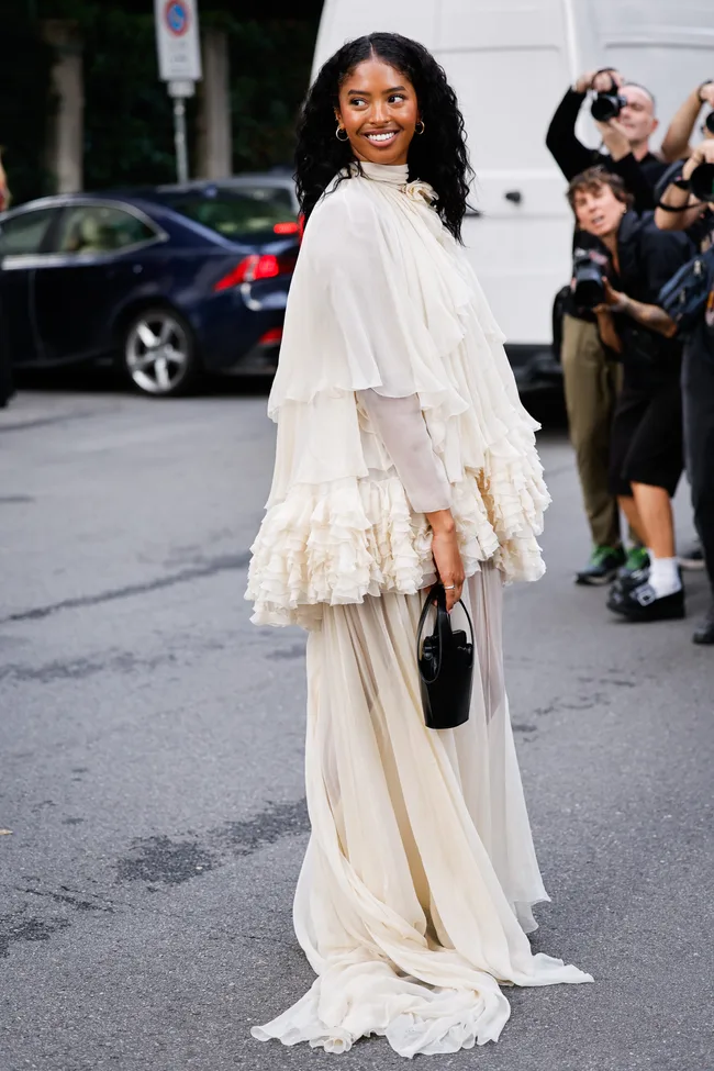 Natalia Diamante Bryant is seen wearing a cream-colored tiered dress with multiple layers of cascading ruffles and a small structured black bag outside Alberta Ferretti fashion