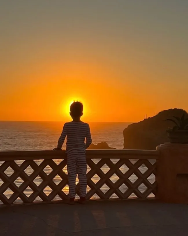 prince harry and meghan's son Archie stands on a balcony watching the sun set over the ocean