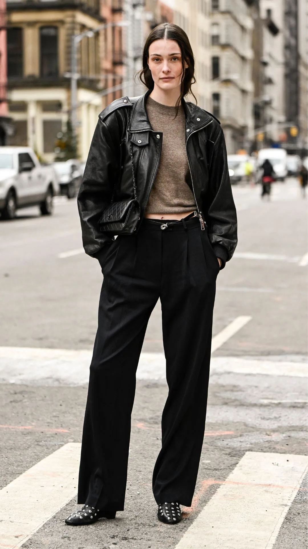 woman wears leather jacket and black trousers with black studded ankle boots