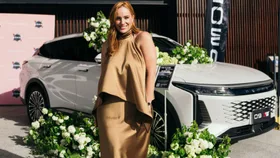 Jules Robinson at SXSW Omoda panel wearing gold dress car in background