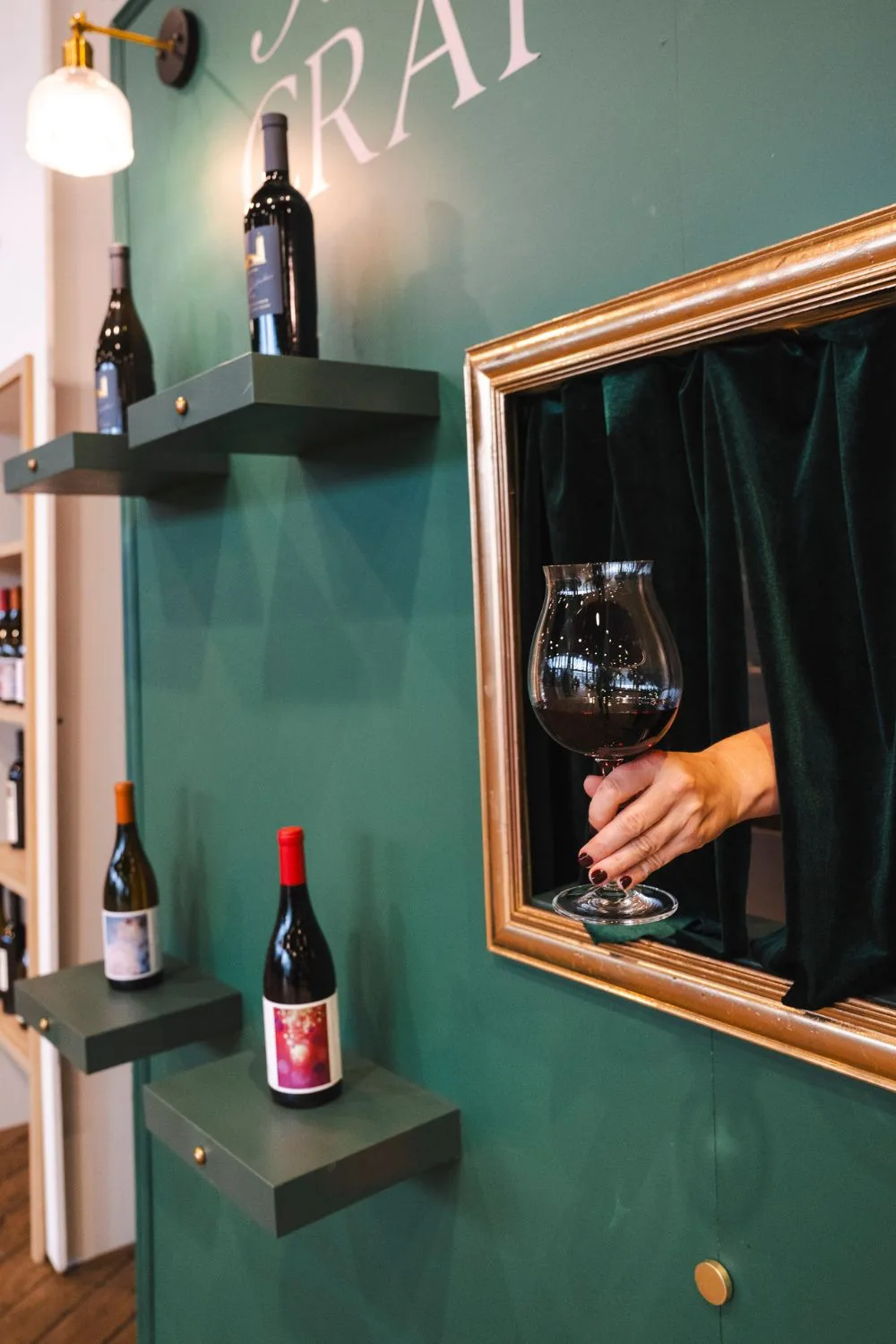 A green wall display of wine with hand presenting a glass