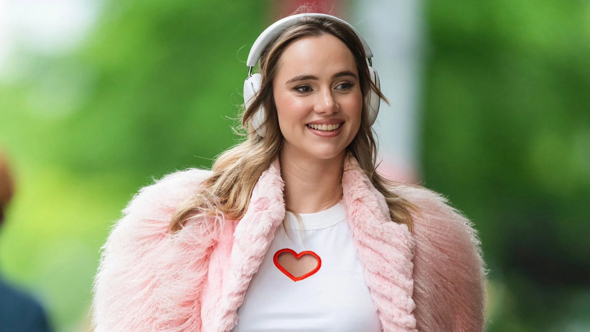 Suki Waterhouse wearing pink fur coat and headphones 