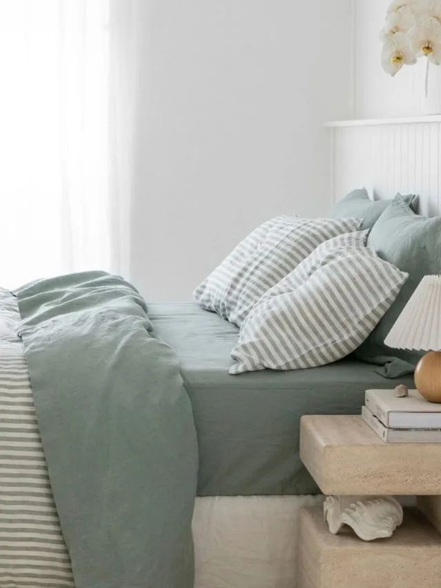 Blue-green bed with block-coloured sheets and striped quilt cover and decorative pillows from I Love Linen