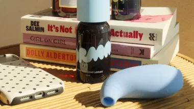 A new clitoral suction sex toy for women lies on a table with some lubricant and a stack of women's books