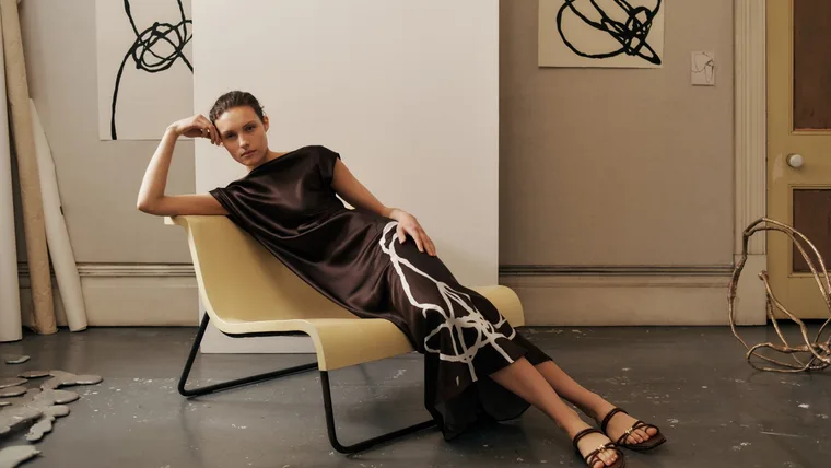 Camie Lyons lounges on minimal 1960s inspired yellow armchair while wearing brown silk dress for Trenery campaign