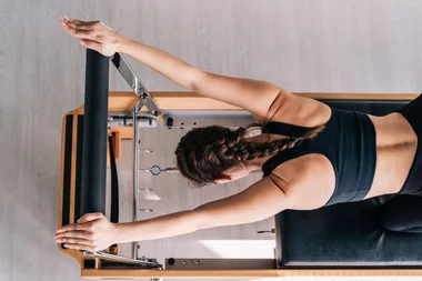 Slender beautiful woman doing Pilates on reformer machines on a sunny day. Top view.