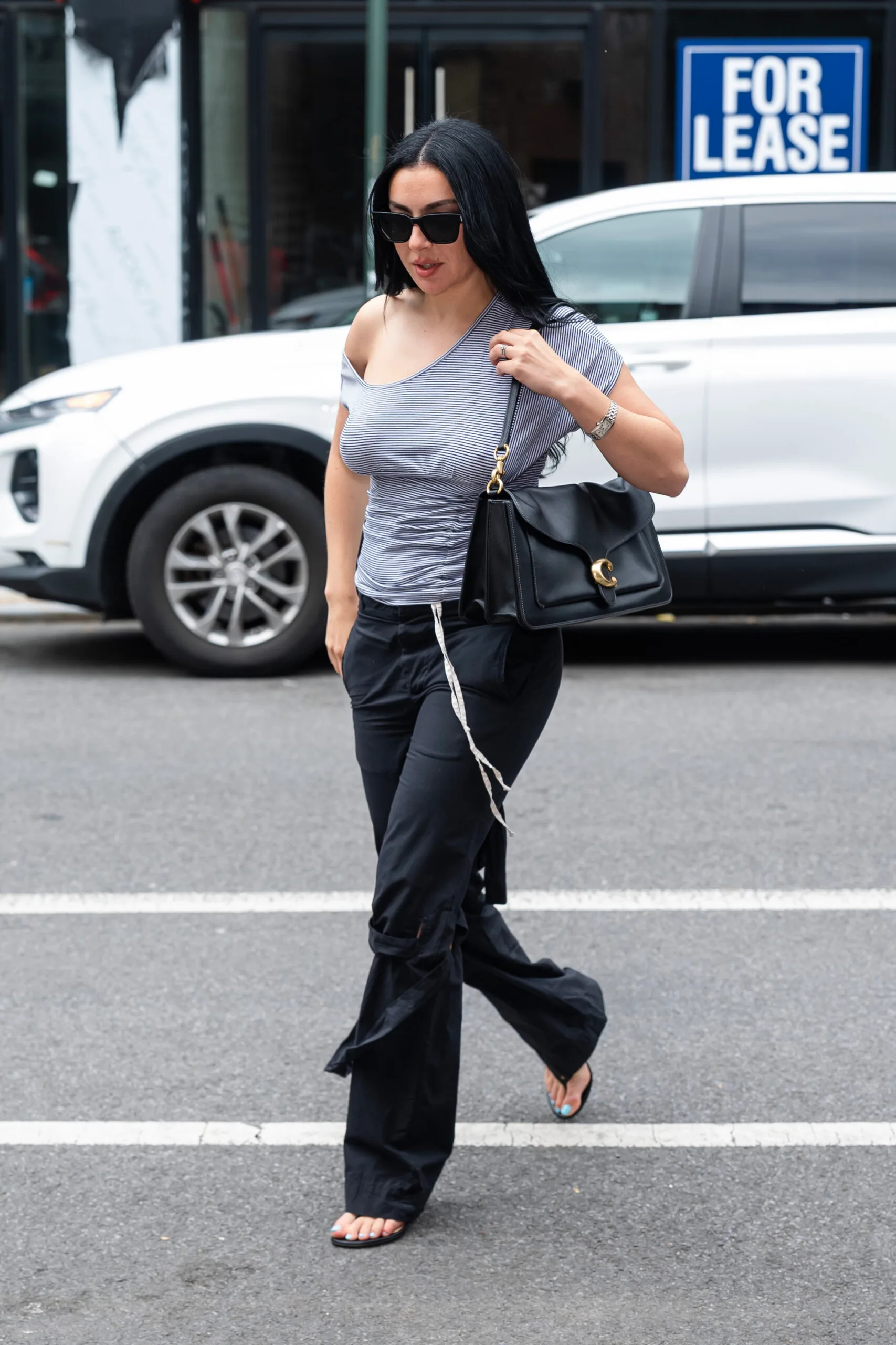 Singer Charli XCX carries a large Coach Tabby Bag in black, while wearing black pants, a striped off-shoulder top.