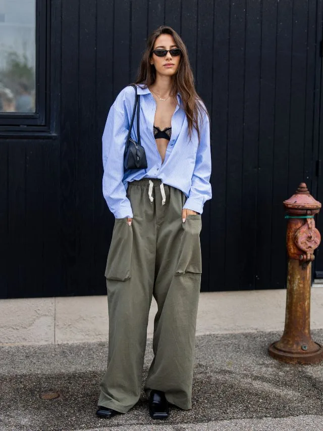 Woman wearing casual, khaki drawstring pants at fashion week with a blue striped shirt and exposed lacy black bra