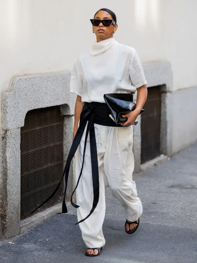 A woman with white drawstring pants, thick black tie belt and white satin top demonstrating how to style drawstring pants to work