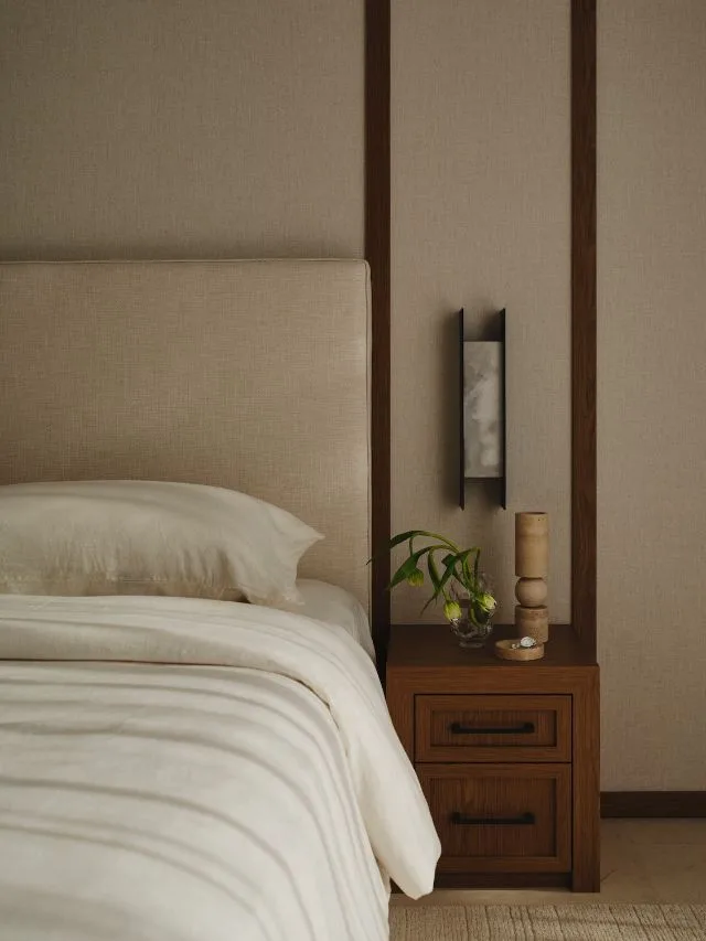 An oatmeal linen upholstered headboard bed with cream bedding a chestnut timber side table