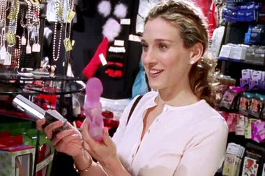 Carrie Bradshaw shopping at a store, notably holding a vibrator while smiling, from "Sex and the City."