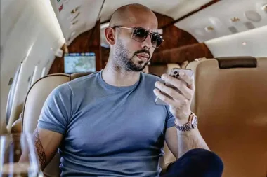 Man in sunglasses and blue shirt looking at smartphone while sitting in a luxurious private jet.