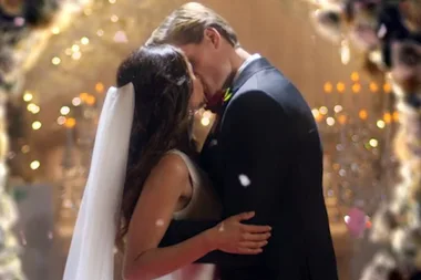 "A bride and groom kiss at their wedding with warm, sparkling lights in the background."