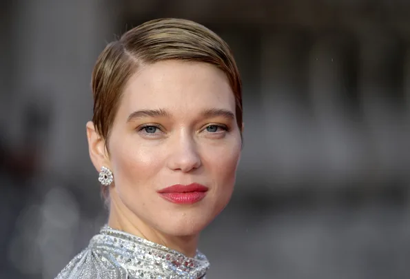 A woman with short brown hair, wearing diamond earrings and a sparkling silver dress, posing outdoors.