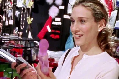 A woman smiling while holding a pink vibrator in a store scene from "Sex and the City."