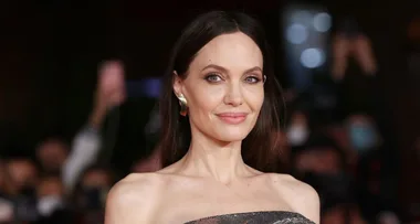 "Smiling woman with long dark hair in a strapless dress and gold earring at a formal event."