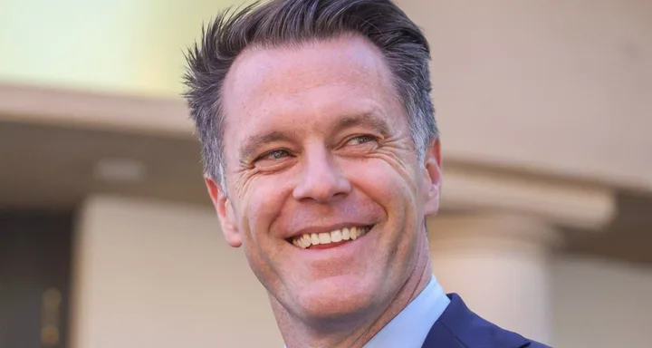 A smiling man in a suit with short hair stands outdoors.