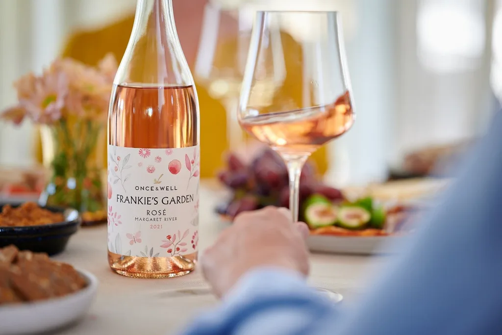 bottle of rose wine and glass of rose wine on a table with food in the background