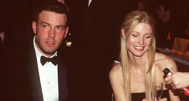 Two people in formal attire at an event, a man in a tuxedo and a woman smiling while holding a champagne glass.