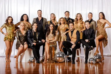 Group photo of "Dancing with the Stars" Australia 2024 contestants in gold and black outfits, posing with disco balls on wooden floor.